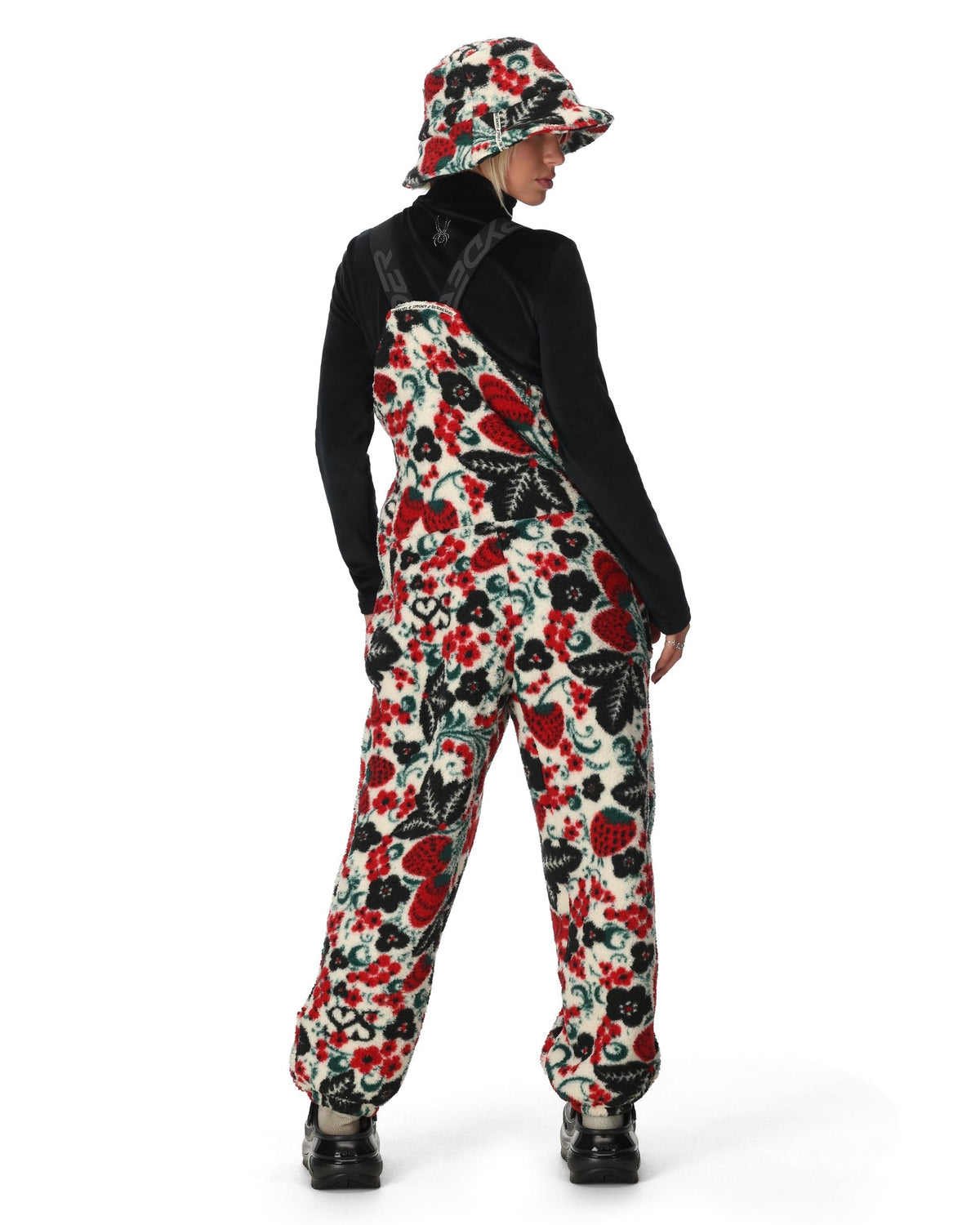 Person wearing a floral patterned jumpsuit and hat on a white background