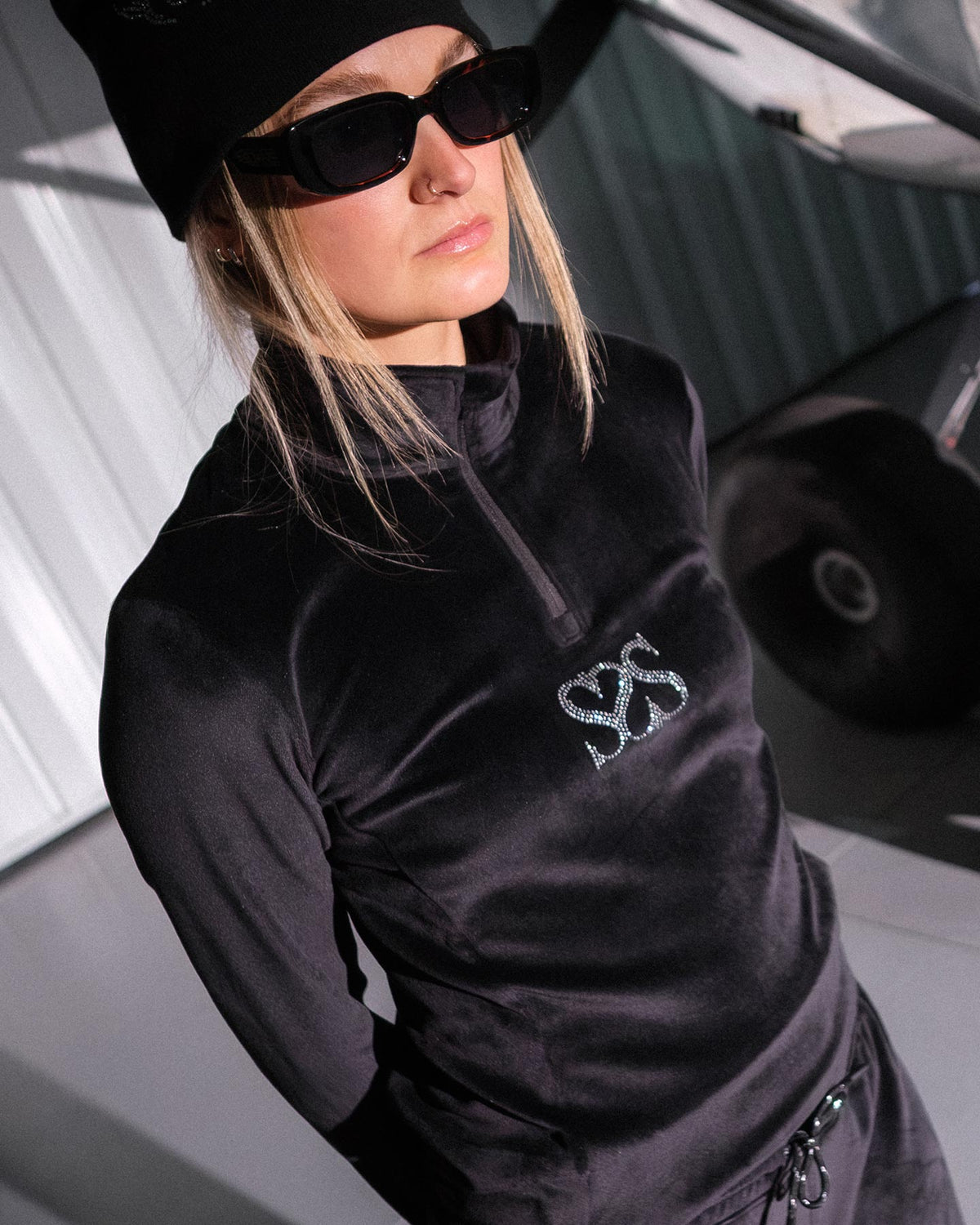 Person wearing a black jacket with a logo, standing next to a vehicle.