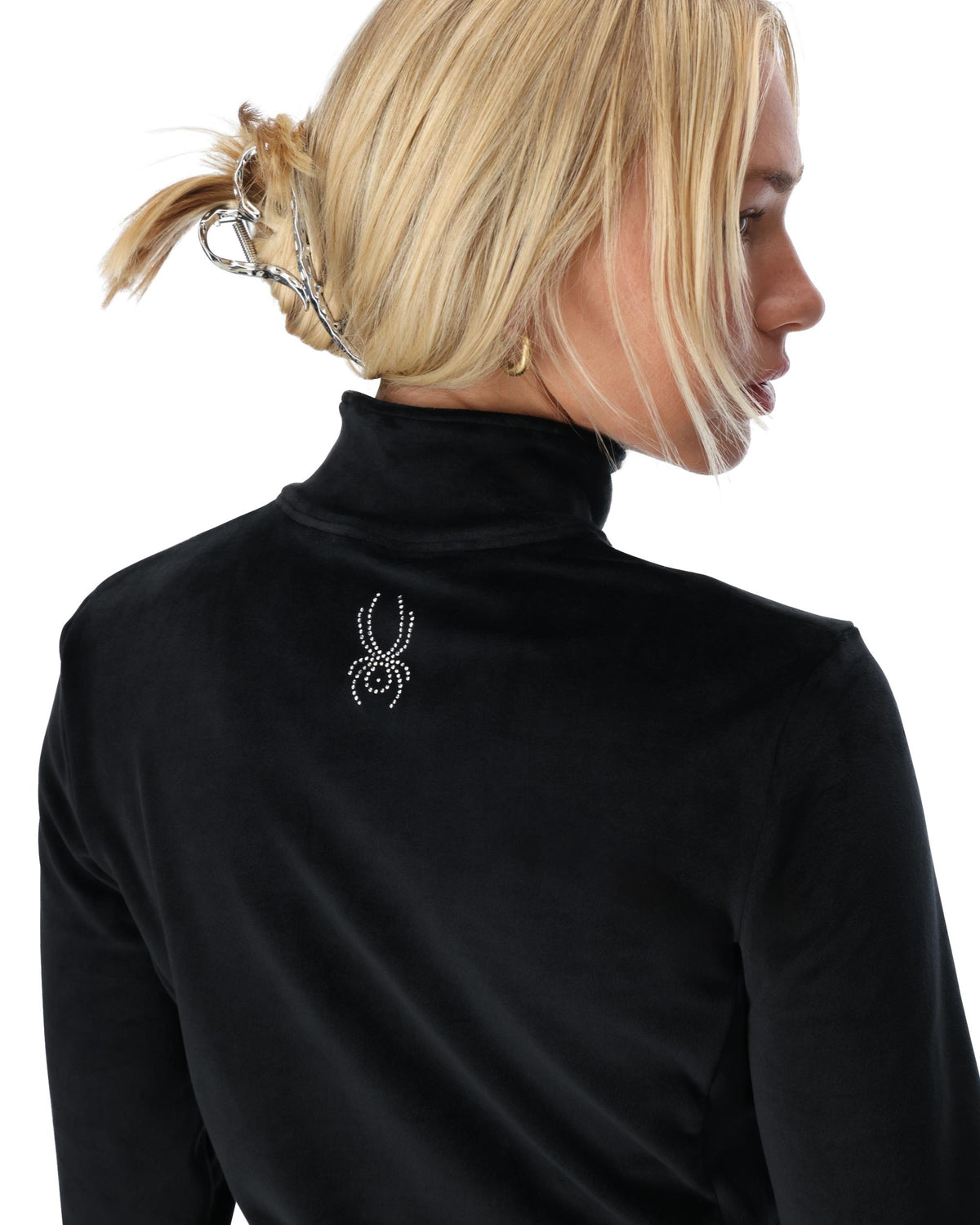 Person wearing a black turtleneck with a decorative spider emblem on a white background