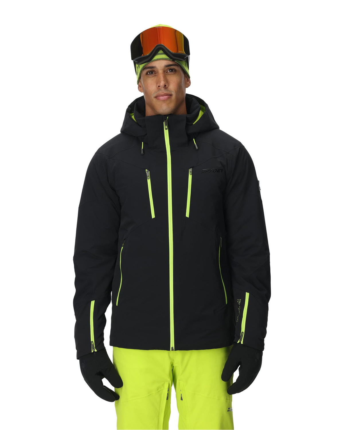 Person wearing a black ski jacket with green accents, goggles, and yellow pants on a white background