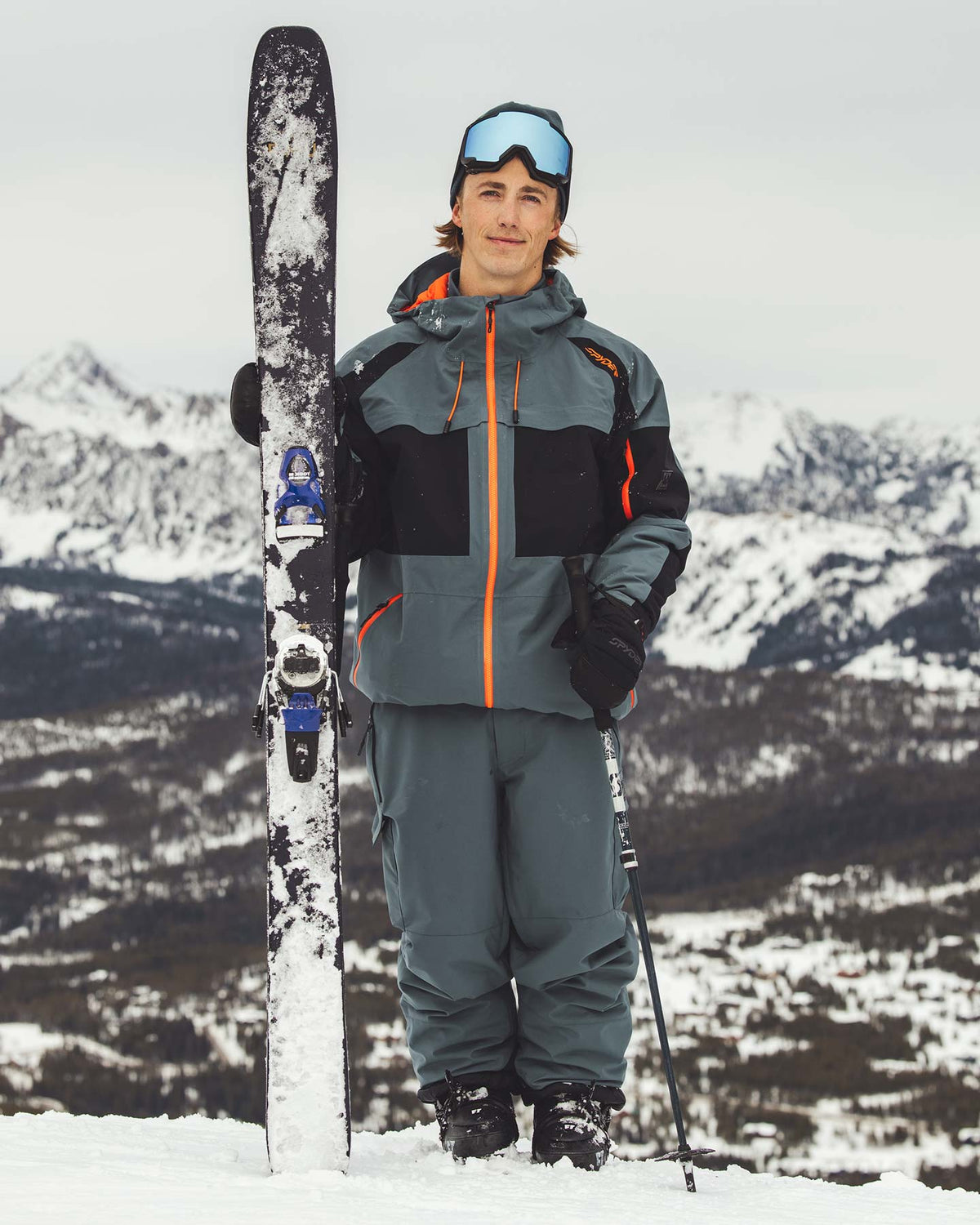 Person in ski gear holding a ski with a mountainous background