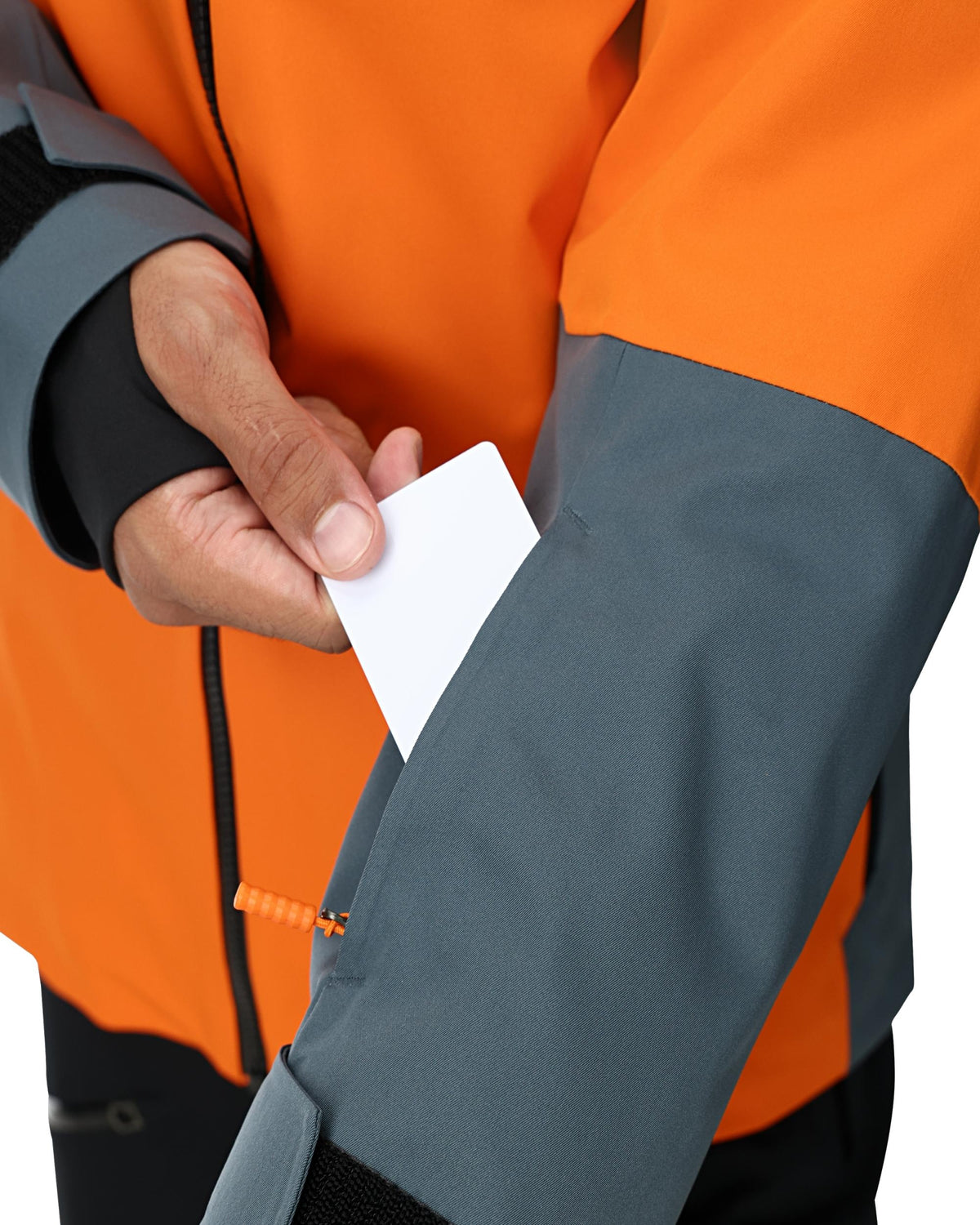Person wearing an orange and gray jacket with a hand holding a white card.