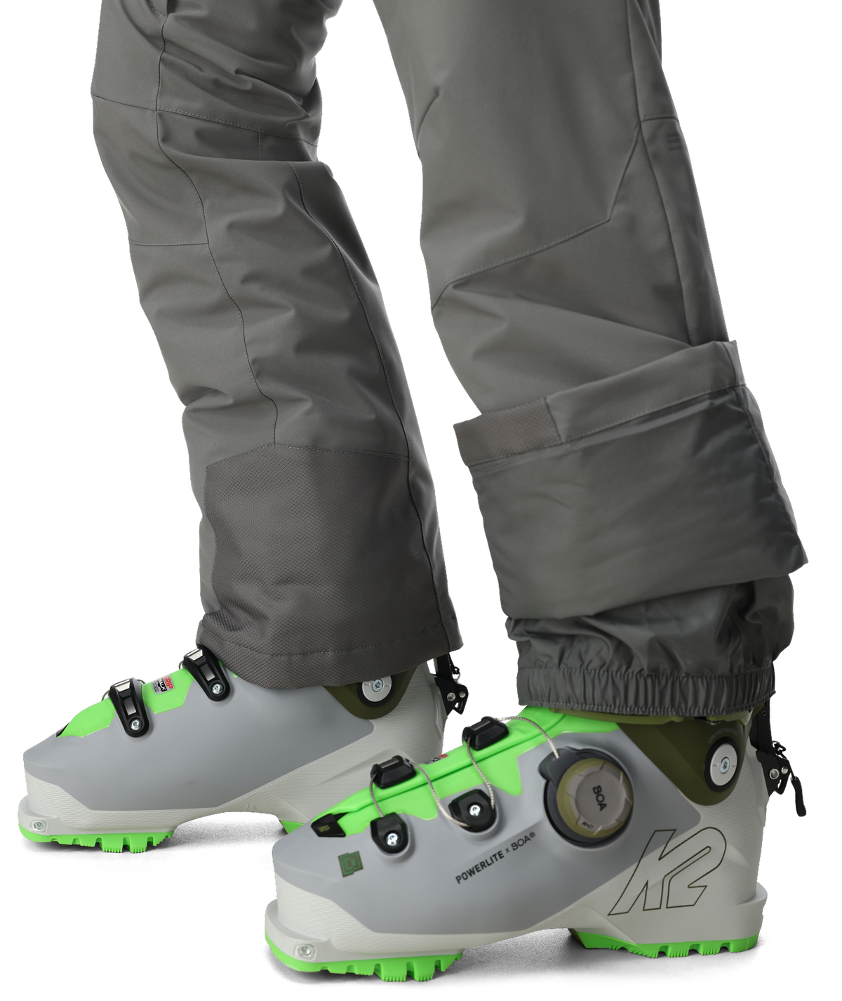 Gray ski boots with green accents worn with gray pants on a white background