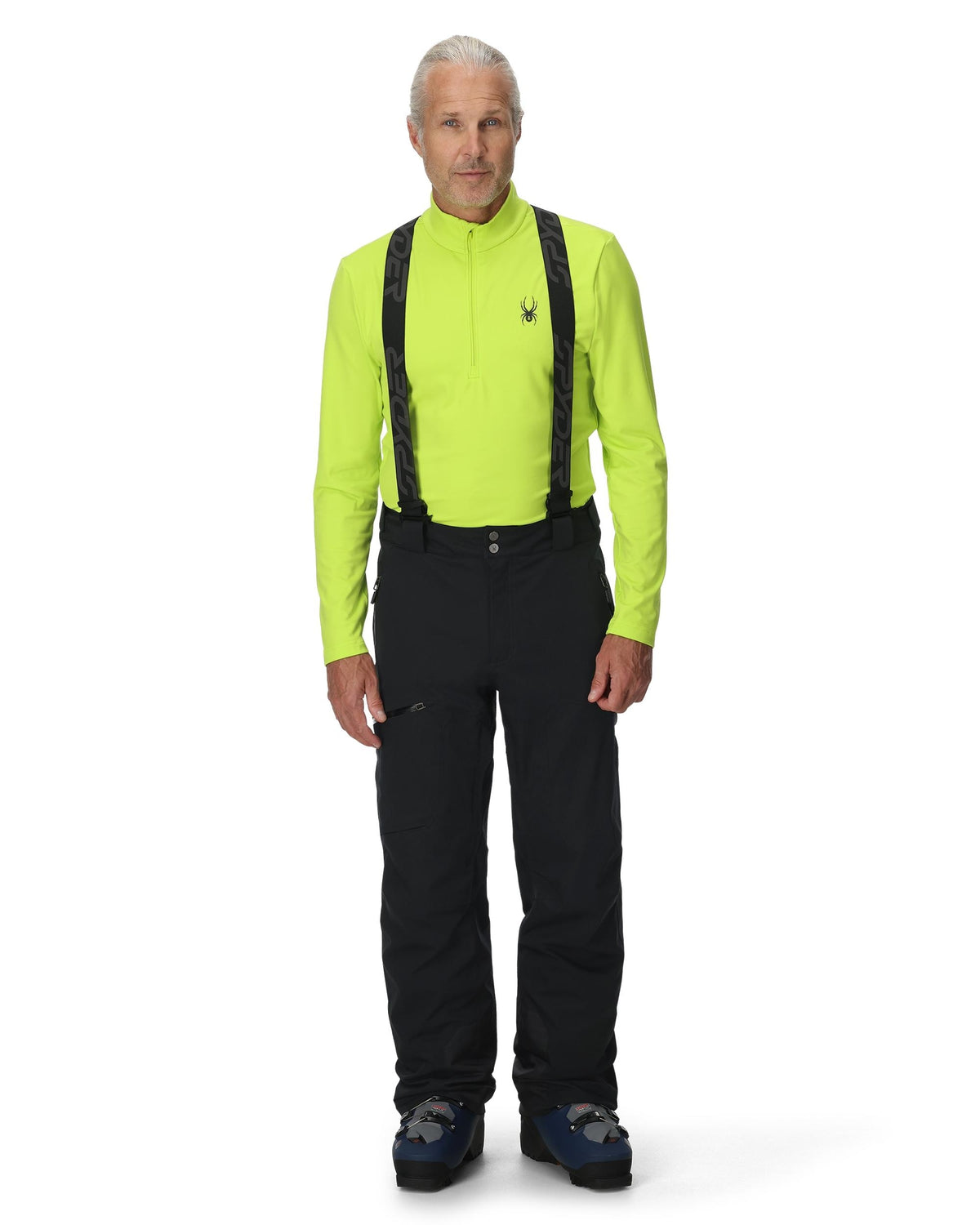 Man wearing a bright green jacket, black pants, and suspenders on a white background
