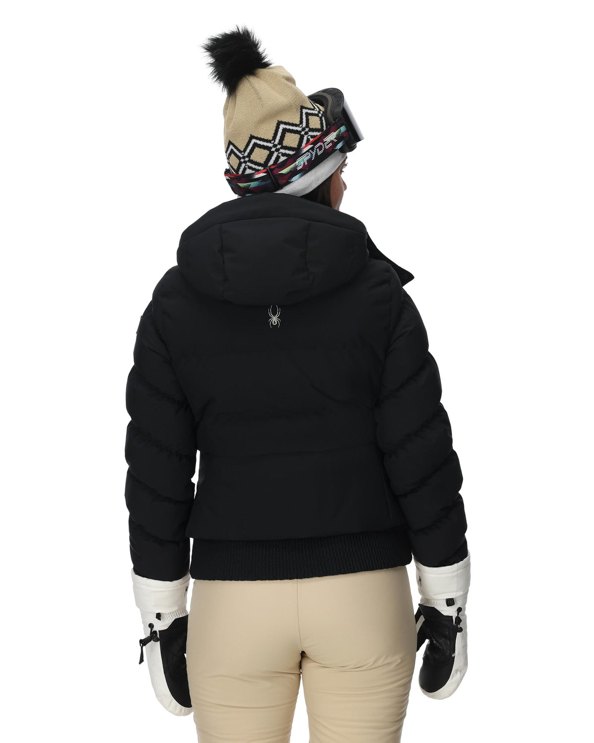 Person wearing a black puffer jacket, beige pants, and a patterned beanie on a white background