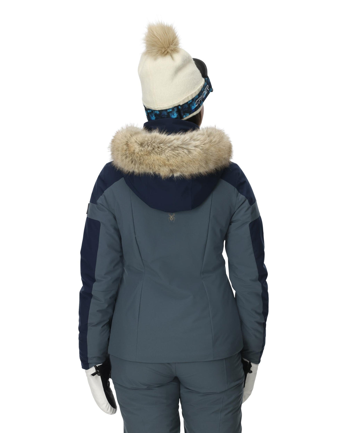 Person wearing a blue winter jacket with fur-lined hood and matching pants on a white background