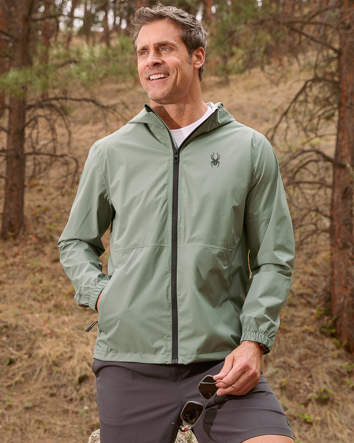 Man wearing a green jacket with a brand logo in a forest setting