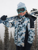 Person wearing a camouflage ski jacket and holding skis with a snowy background
