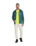 Man wearing a green jacket with a brand logo, yellow shirt, and white pants on a white background