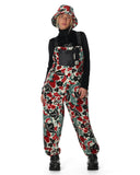 Person wearing a colorful floral patterned bib overalls with a black turtleneck and bucket hat on a white background.