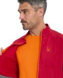 Man wearing a red jacket with a logo, orange shirt underneath, on a white background
