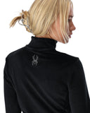 Person wearing a black turtleneck with a decorative spider emblem on a white background
