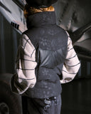 Person wearing a black and gray patterned jacket with a hood, standing inside a vehicle.