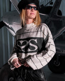 Person wearing a sweater with a logo, standing in front of a vehicle.