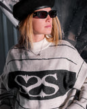 Person wearing a black and gray patterned sweater with sunglasses and a cap.