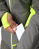 Person wearing a gray and green jacket holding a white card.