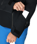 Person wearing a black jacket with a pocket, holding a white card.