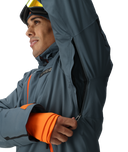 Person wearing a gray jacket with orange accents, standing against a white background