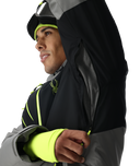 Person wearing a black and gray jacket with neon green accents on a white background