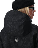 Person wearing a black patterned jacket with a spider logo, black beanie, and sunglasses on a white background