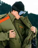 Person wearing a green jacket with orange accents and goggles, standing outdoors.