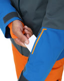 Person wearing a blue and orange jacket with a hand holding a white card.