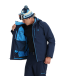 Person wearing a blue ski jacket with a hood, goggles, and a beanie on a white background