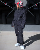 Person wearing a black snowsuit and colorful cap standing in front of an airplane.
