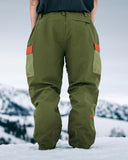 Person wearing green snow pants with orange accents in a snowy landscape