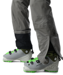 Gray ski boots with green accents worn by a person in gray pants on a white background