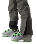 Gray ski boots with green accents worn with gray pants on a white background