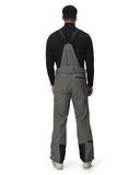 Person wearing gray bib overalls with black sleeves on a white background