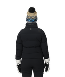 Person wearing a black puffer jacket, black pants, white gloves, and a patterned beanie on a white background