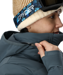 Person wearing a blue jacket and a beanie with Spyder logo, zipping up the jacket.