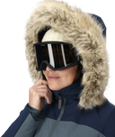 Person wearing a blue winter jacket with a fur-lined hood and black goggles on a white background