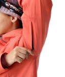 Person wearing a coral jacket with a brand logo on a white background