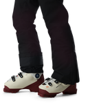 White ski boots with red soles worn with black pants on a white background