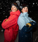Two women in Spyder shell jackets  standing back-to-back with snow falling around them.
