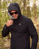 Man wearing a black jacket with a hood in a forest setting