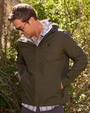 Man wearing a green jacket outdoors with greenery in the background